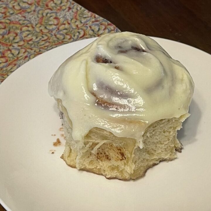 freshly baked and iced sourdough cinnamon roll on a white plat
